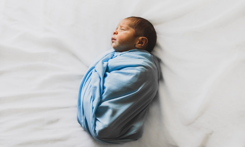 Baby photoshoot lying on bed wrapped in blue cloth