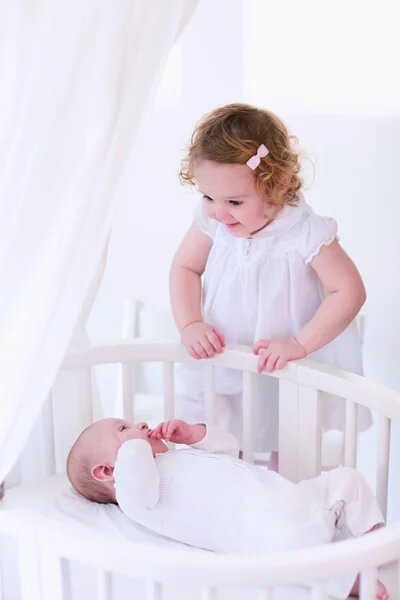 bigger sister looking at newborn baby in crib photoshoot